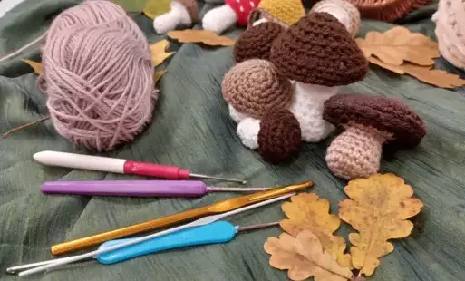 Na zdjęciu szydełka, wełna i grzybki wykonane na szydełku.